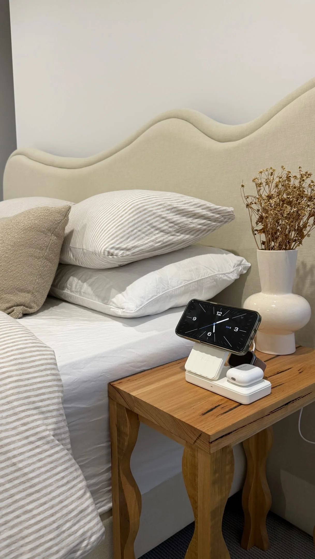 Timber bedside table with wavy legs holding our charger and a vase
