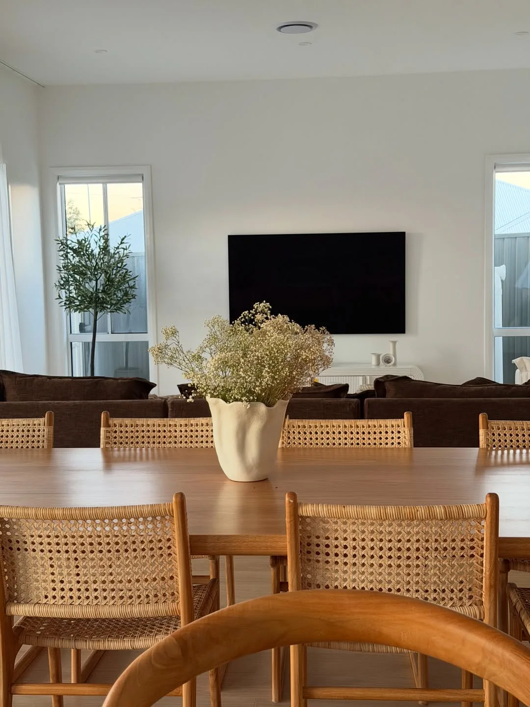 Our custom timber dining table styled with a ceramic vase and woven dining chairs